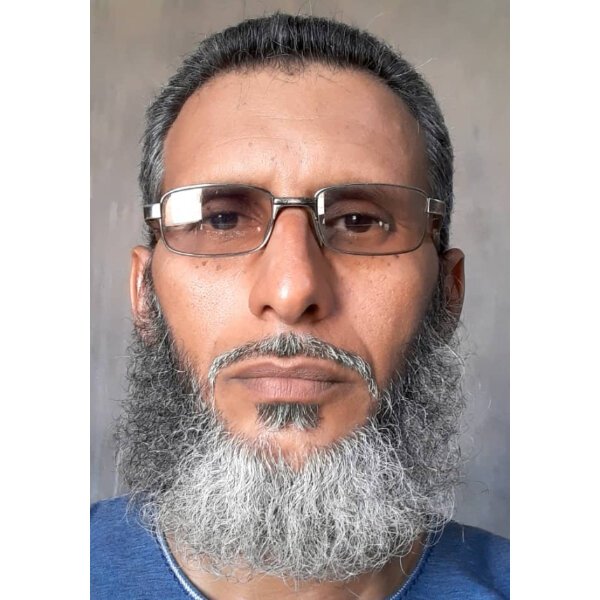 Islamic Center A man with short gray hair, a full gray beard, glasses, and a blue shirt looks directly at the camera against a plain background. Islam