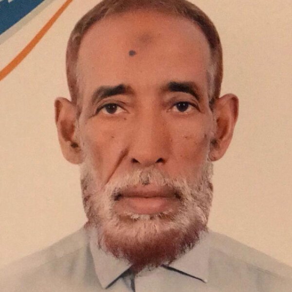 Islamic Center An older man with a short gray and brown beard, wearing a light-colored shirt, looks directly at the camera against a neutral background with a curved orange and blue line. Islam