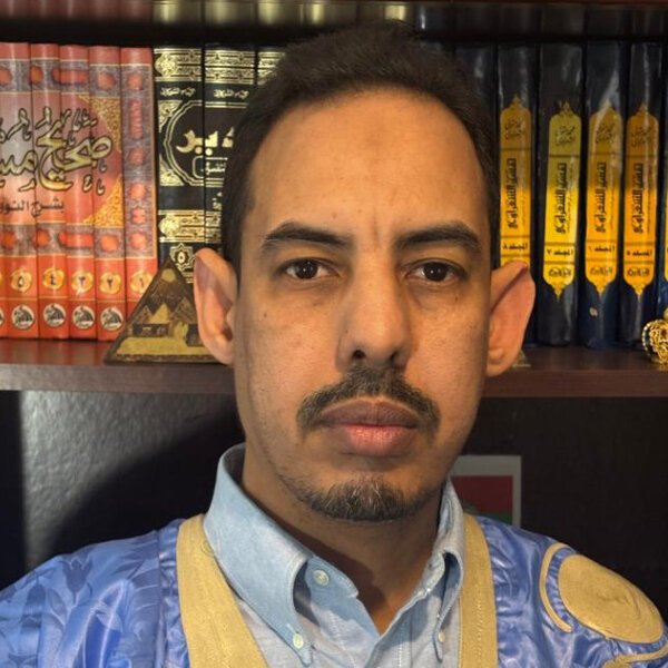 Islamic Center A man with short hair and a trimmed mustache and beard poses in front of a bookshelf filled with Arabic books. Islam