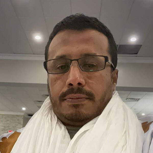 Islamic Center A man wearing glasses and a white scarf looks at the camera in a well-lit indoor setting with a tiled ceiling. Islam