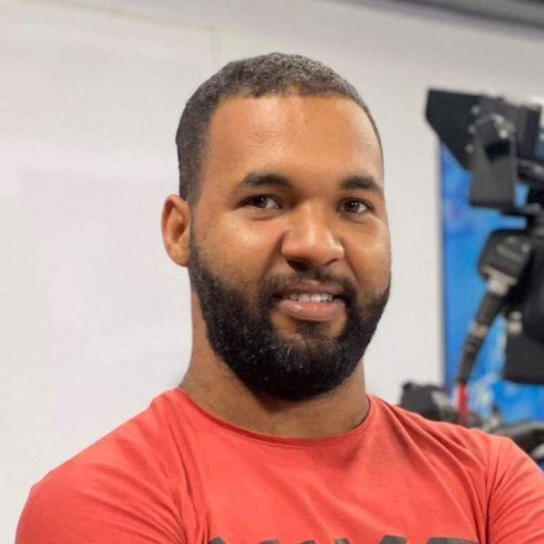 Islamic Center A man with a short beard and short hair wearing a red t-shirt stands indoors with a camera and equipment visible in the background. Islam