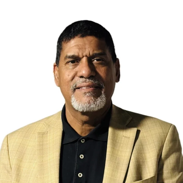 Man with short hair and a goatee wearing a tan blazer over a black collared shirt, facing forward against a plain white background.
